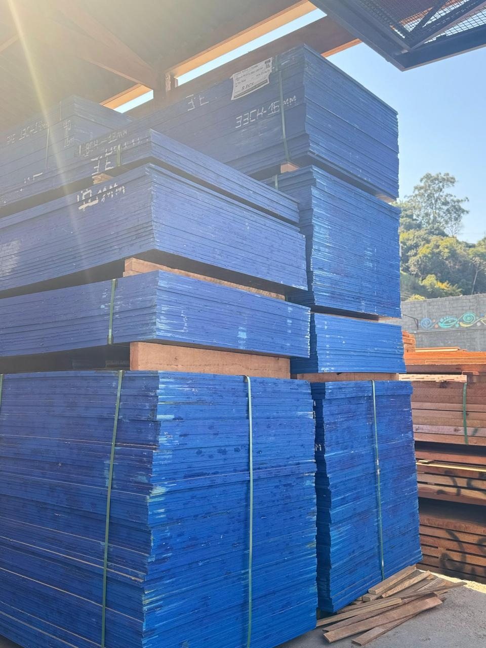 Pilhas de Madeirit plastificado azul no pátio da Rocha Telhas